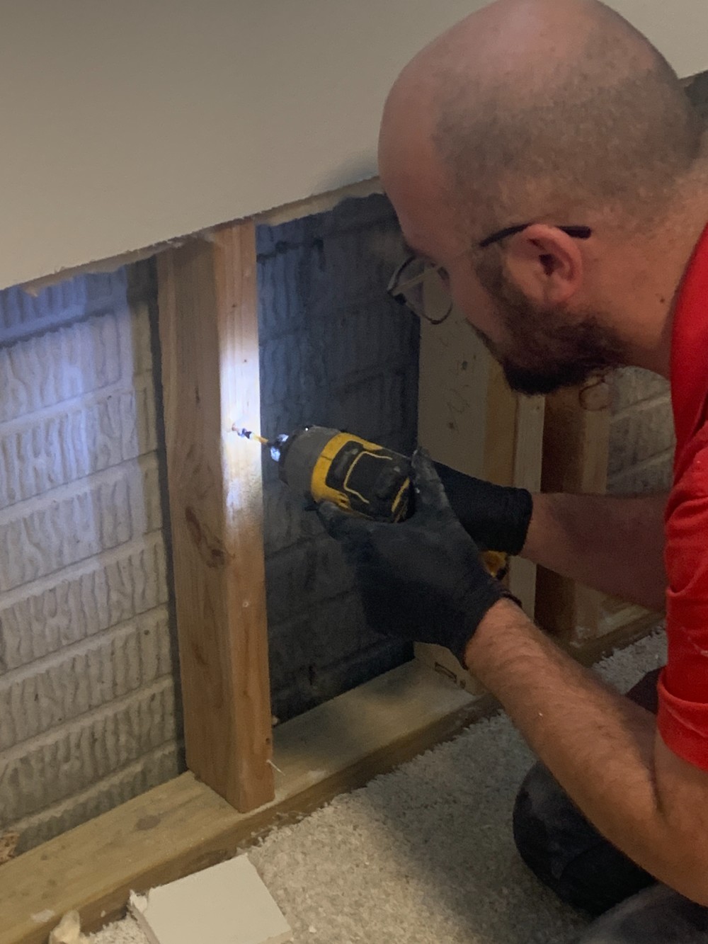 Technician drilling into a wooden wall frame during an interior renovation.