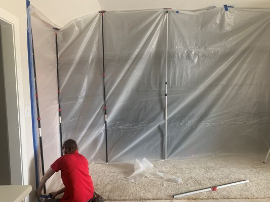 Restoration technician setting up plastic containment barriers in a residential room.