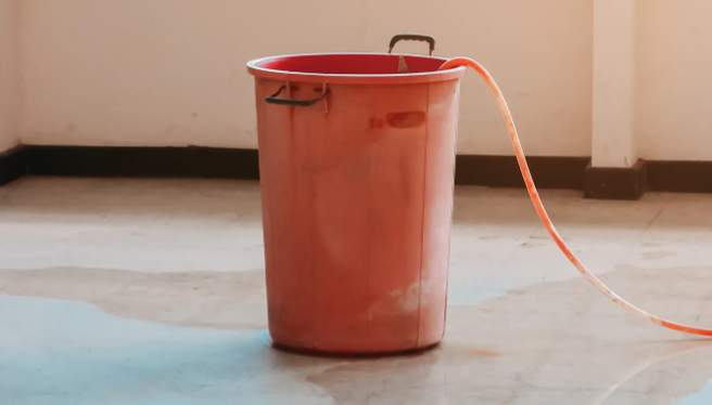 Bucket on the floor of a commercial building with extensive water damage.