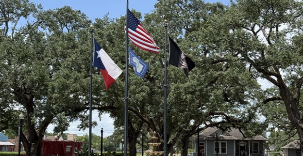 League Park in League City, Texas, viewing the fountain and flagpoles with historic buildings in the background.