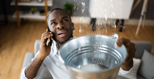 A Mauldin, SC, homeowner calls for water damage restoration help while holding a bucket collecting water coming from the ceiling.