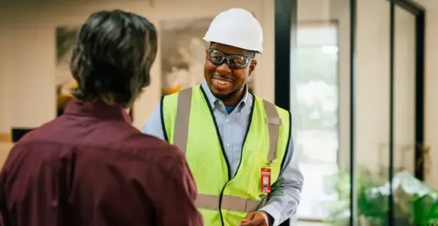 A Rainbow Restoration service professional wearing a hard hat and vest speaking with a customer.