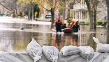 Sandbags with two people in the distance wading in water.