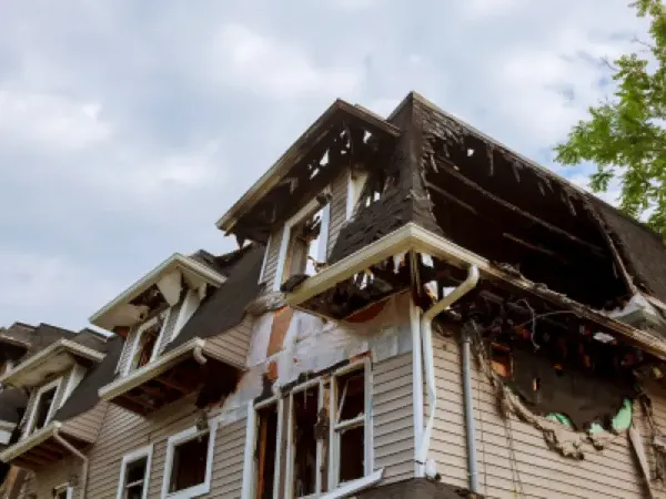 Fire-damaged home with heavy smoke and structural damage to the roof and upper floors after a house fire.