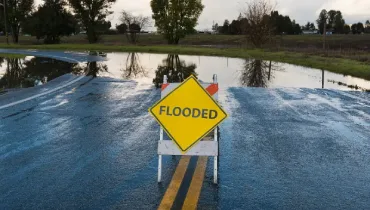 A flooded roadway with standing water and a warning sign illustrates the type of water damage Johnson City homeowners and businesses may face after heavy rain or plumbing failures.