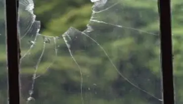 Close-up of a broken window with a large hole and visible cracks.