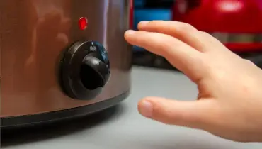 Hand reaching for dial on crockpot.