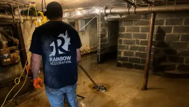A Rainbow Restoration service professional removes standing water from a flooded basement using professional extraction equipment.