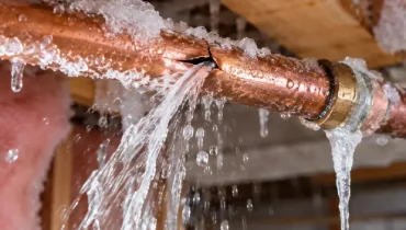 A frozen copper pipe has burst, spraying water into the surrounding framing after freezing temperatures.