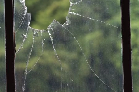 Close-up of a broken window with a large hole and visible cracks.