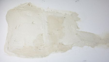 Discoloration and patchy staining on a white wall, showing signs of water damage or moisture intrusion. The affected area appears uneven and textured, indicating possible seepage behind the surface.