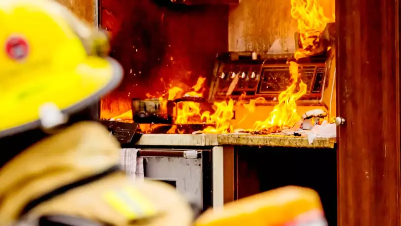 A firefighter in the foreground with a burning kitchen in the background.