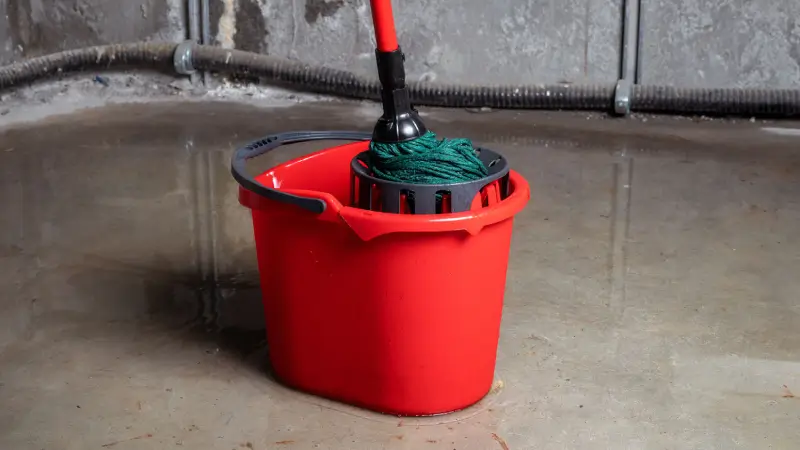 A red bucket and mop sit in a flooded basement. 