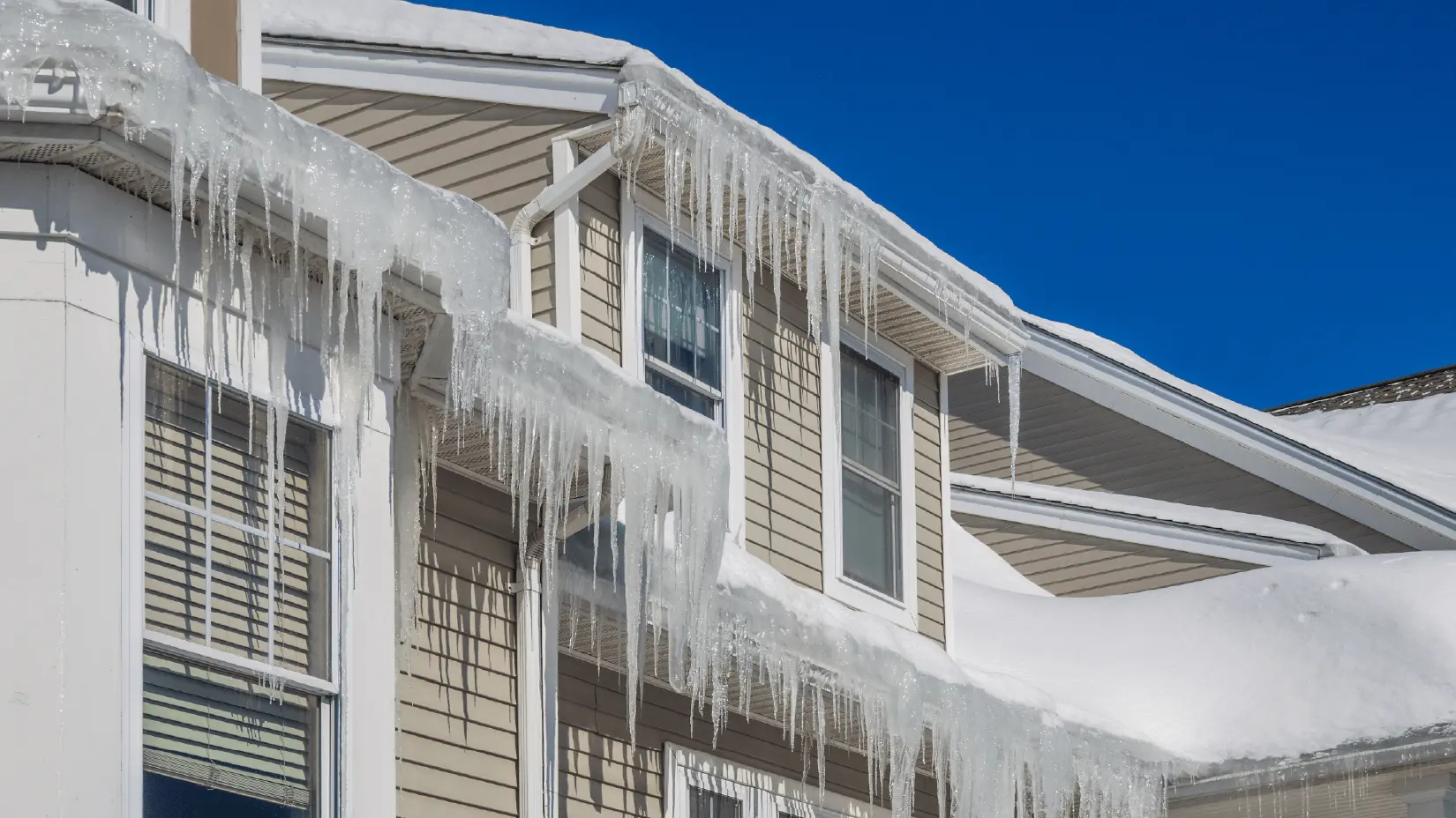 House with ice dam and long icicles hanging from roof. 